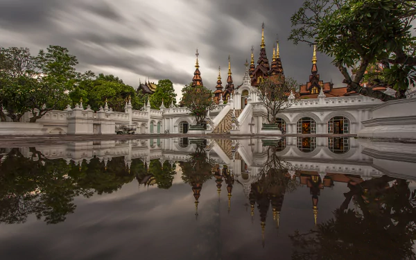 Time-lapse architectural photograph of Chiang Mai, Thailand: ornate temple spires and their reflection in calm water beneath dramatic clouds — 5K Ultra HD PC desktop wallpaper/background.