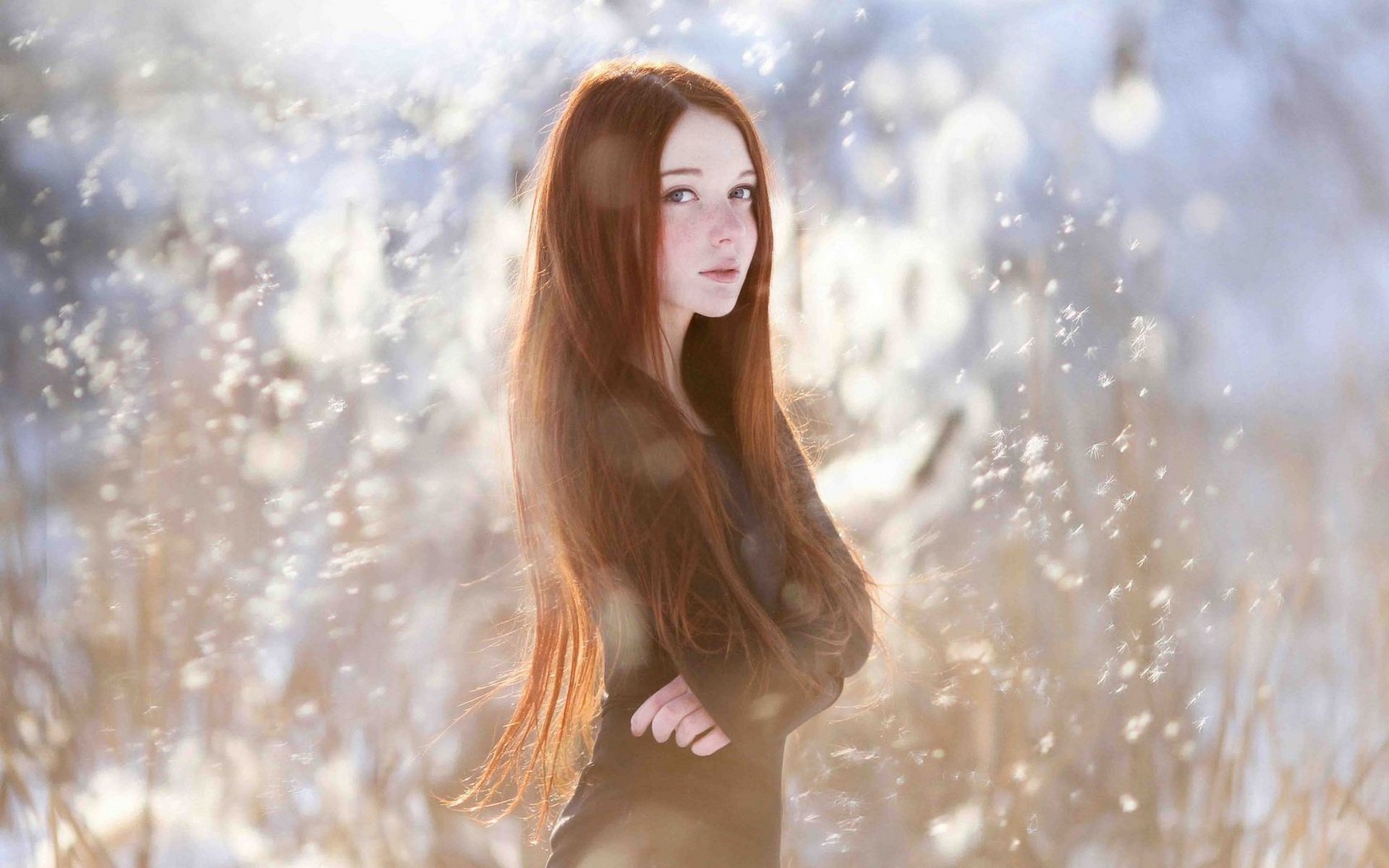 HD desktop wallpaper featuring a woman with long hair in a winter setting, glowing with soft, natural light amid snowy bushes.