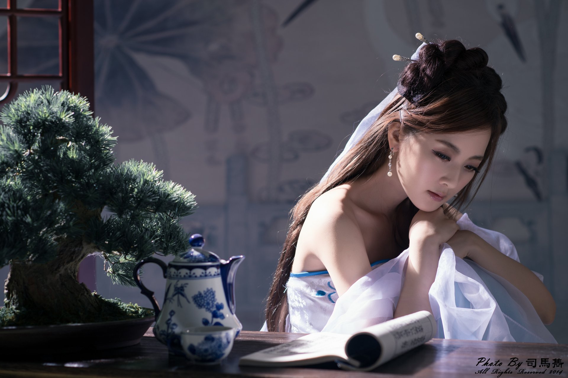 A serene Asian woman adorned with a hairpin gazes thoughtfully at a tea set beside a bonsai tree, immersed in a tranquil atmosphere of Chinese elegance.