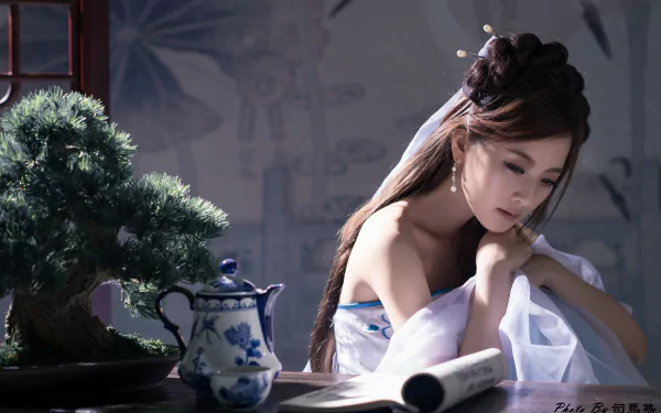 A serene Asian woman adorned with a hairpin gazes thoughtfully at a tea set beside a bonsai tree, immersed in a tranquil atmosphere of Chinese elegance.