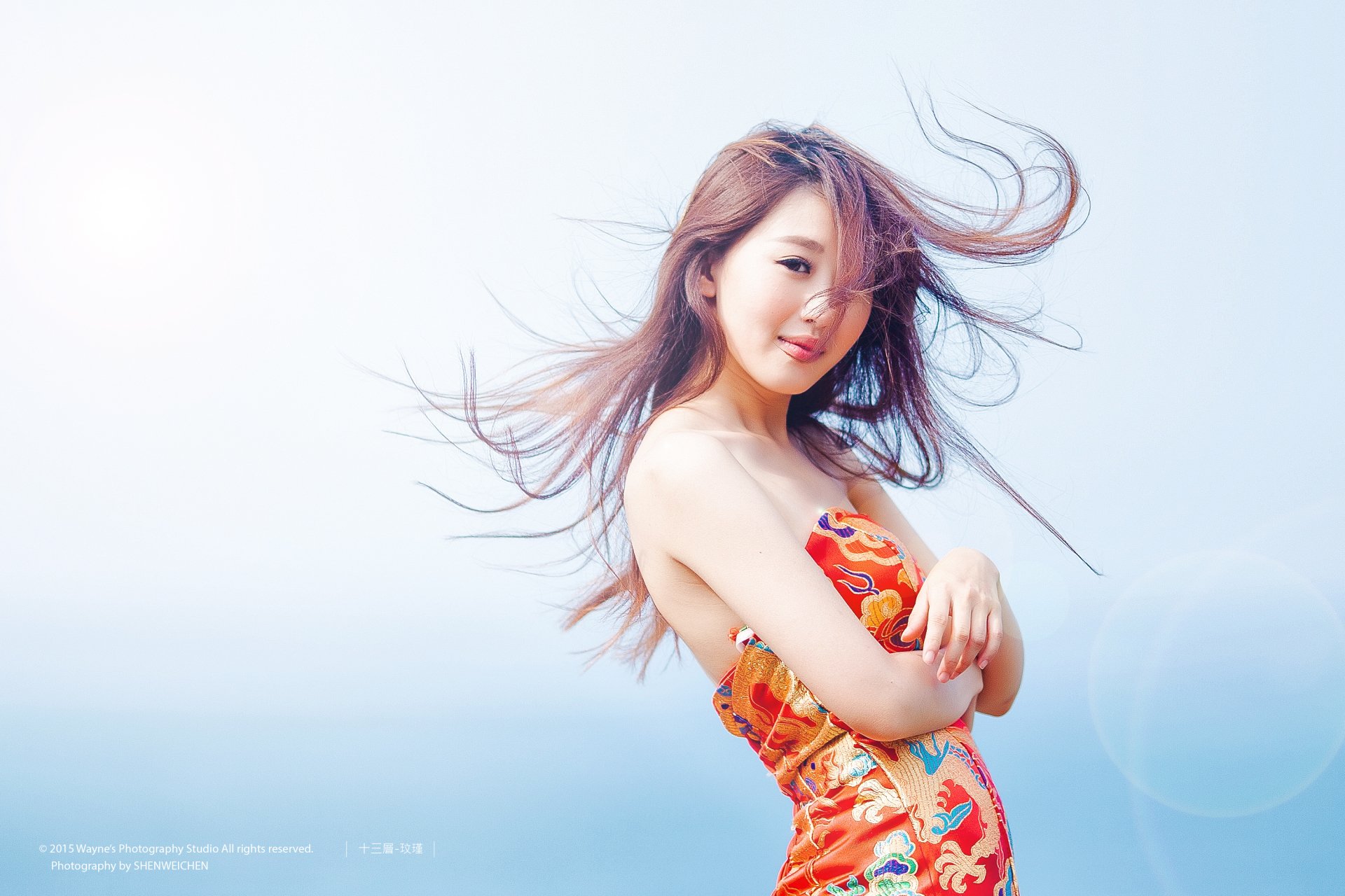 A woman with long hair poses elegantly in a colorful dress against a serene blue background, creating a vibrant and stylish HD desktop wallpaper.