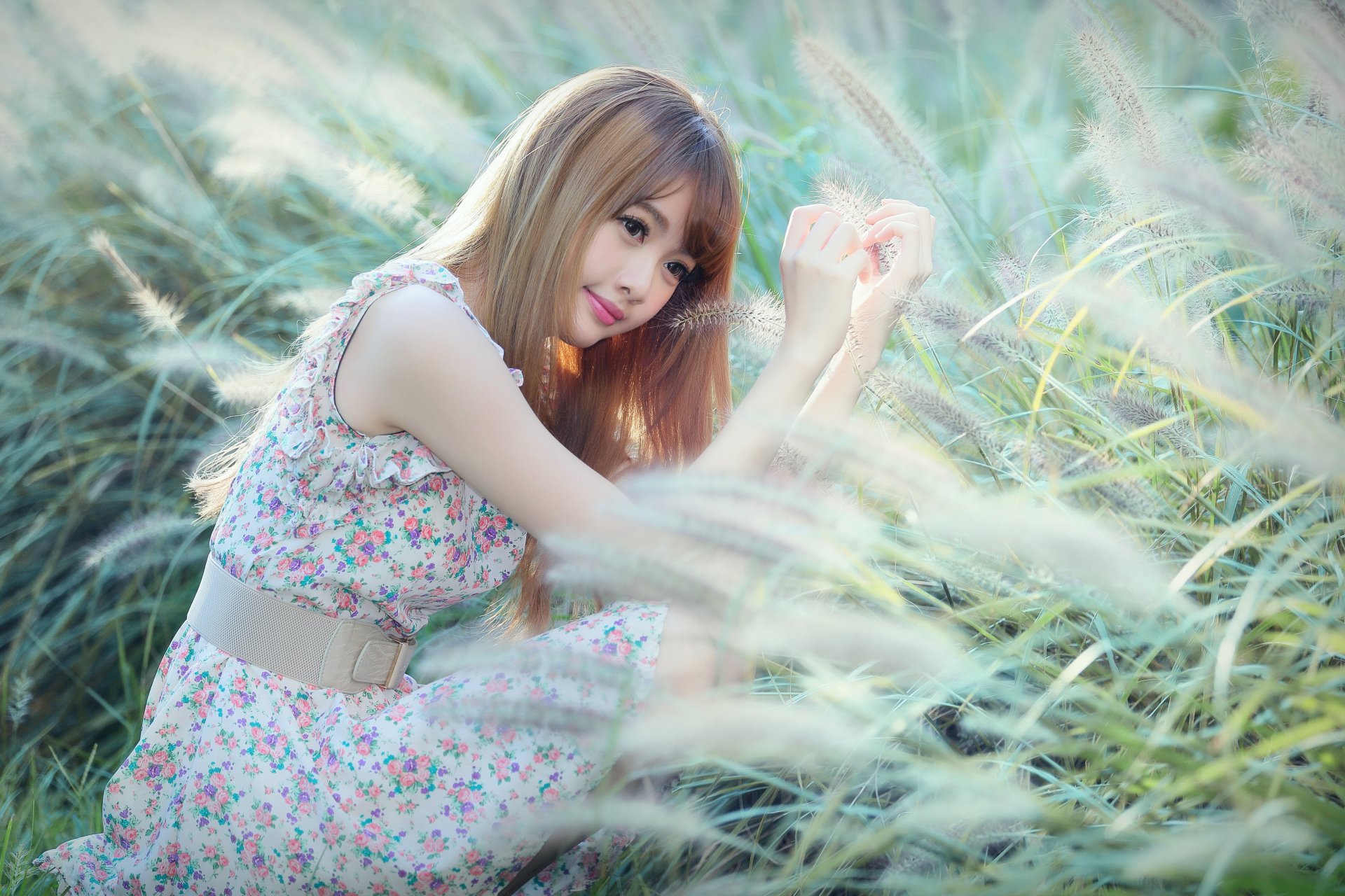 Asian model in a floral dress and belt smiles while sitting in a grassy field, captured in a high-definition portrait. This image, tagged with 'Cubie Wang,' serves as a desktop wallpaper and background.