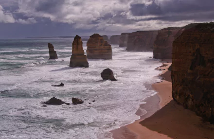 Dramatic ocean waves crash against limestone stacks along the Victoria coastline at The Twelve Apostles, Australia, beneath a cloudy sky in this 4K Ultra HD wallpaper.