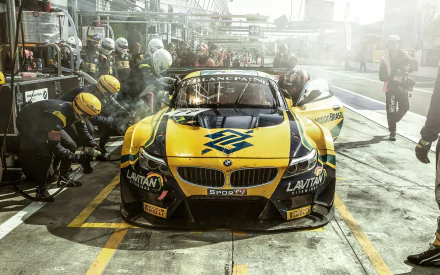 HD wallpaper of a BMW racing car in a dynamic pit stop scene with crew in action.