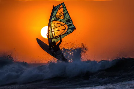 A windsurfer rides a wave against a vibrant orange sunset, captured in stunning 4K Ultra HD, showcasing dynamic watersports action on this PC desktop wallpaper.
