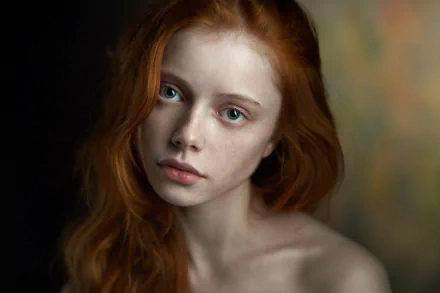 A striking HD desktop wallpaper featuring a woman with blue eyes and flowing red hair, showcasing her captivating face against a softly blurred background.
