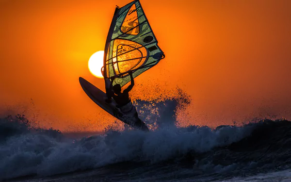 A windsurfer rides a wave against a vibrant orange sunset, captured in stunning 4K Ultra HD, showcasing dynamic watersports action on this PC desktop wallpaper.