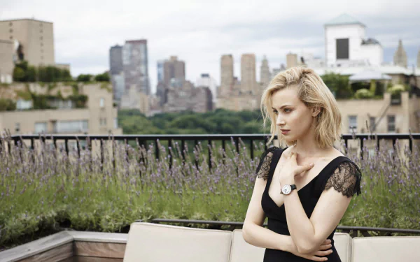Canadian actress Sarah Gadon with blue eyes and blonde hair poses thoughtfully on a rooftop with a cityscape in the background.