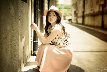 HD wallpaper featuring a Taiwanese woman wearing a hat and skirt, basking in sunlight. The model, Chén Sīyǐng, leans against a wall in an alley, creating a serene and stylish background scene.