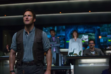 Chris Pratt stands confidently in a control room scene from Jurassic World, surrounded by colleagues, with screens displaying dinosaurs in the background. High-definition desktop wallpaper. 