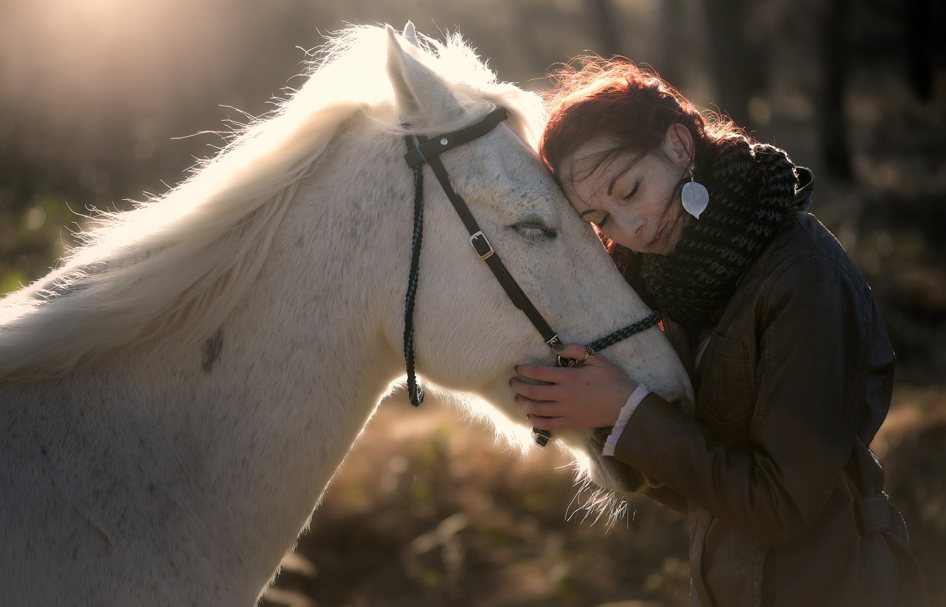 A serene HD wallpaper depicting a red-haired woman with earrings affectionately leaning her head against a white horse in a soft, diffused light, evoking a mood of love and tranquility.