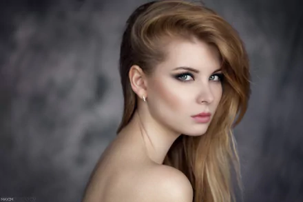 A blonde woman with blue eyes and earrings poses against a soft bokeh background, showcasing her striking features in this HD PC desktop wallpaper.