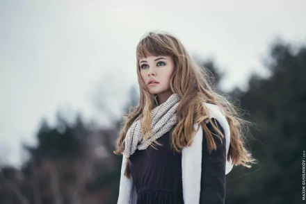 A model with brunette hair and green eyes wears a stylish scarf, standing in a serene outdoor setting, captured in HD as a striking desktop wallpaper.