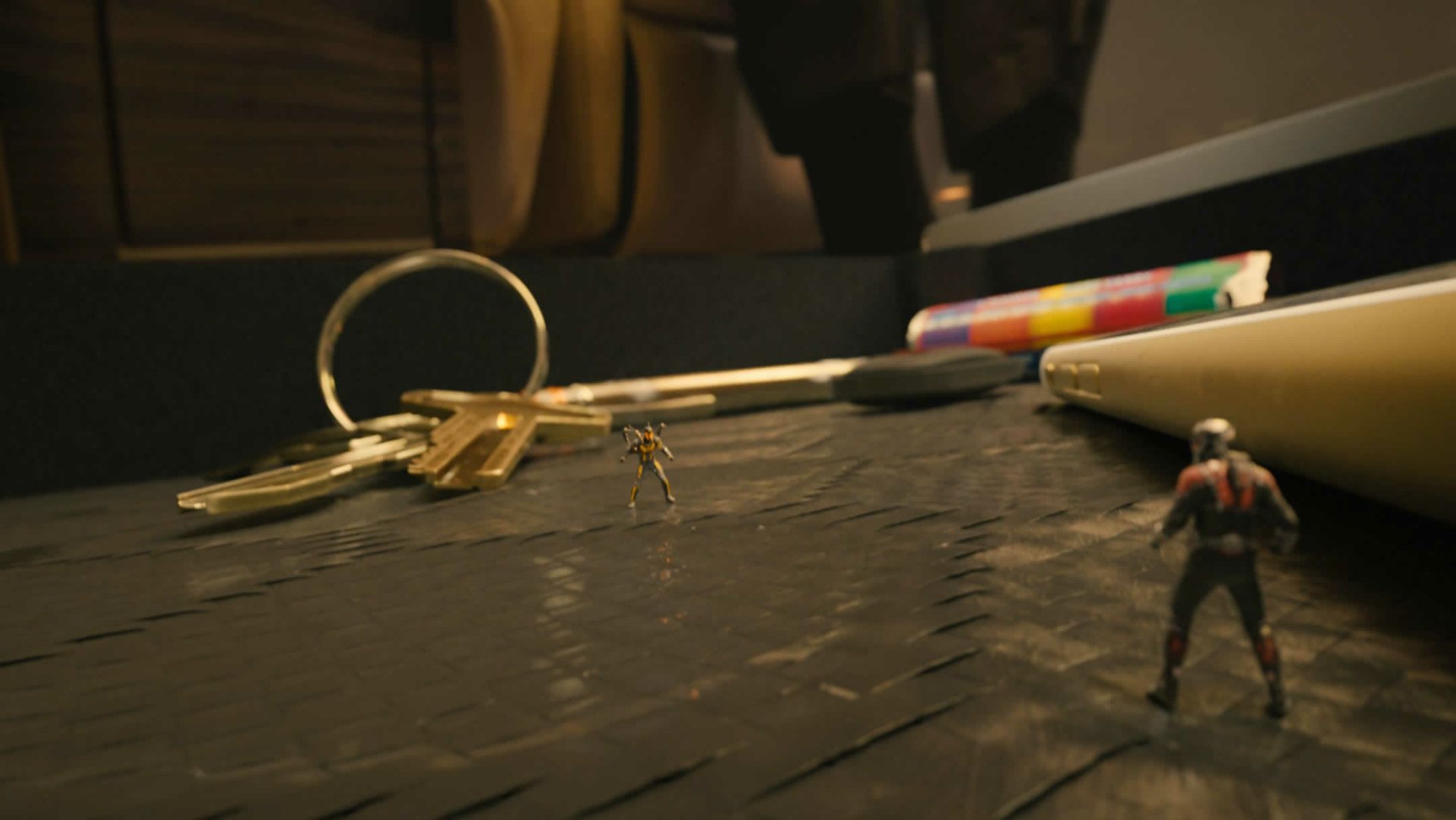 A vibrant HD desktop wallpaper featuring characters from Ant-Man, set against a backdrop of everyday objects like keys and colorful pens, emphasizing their miniature scale.