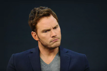 HD desktop wallpaper featuring a man in a navy blue blazer over a grey shirt, with a thoughtful expression, set against a dark background.