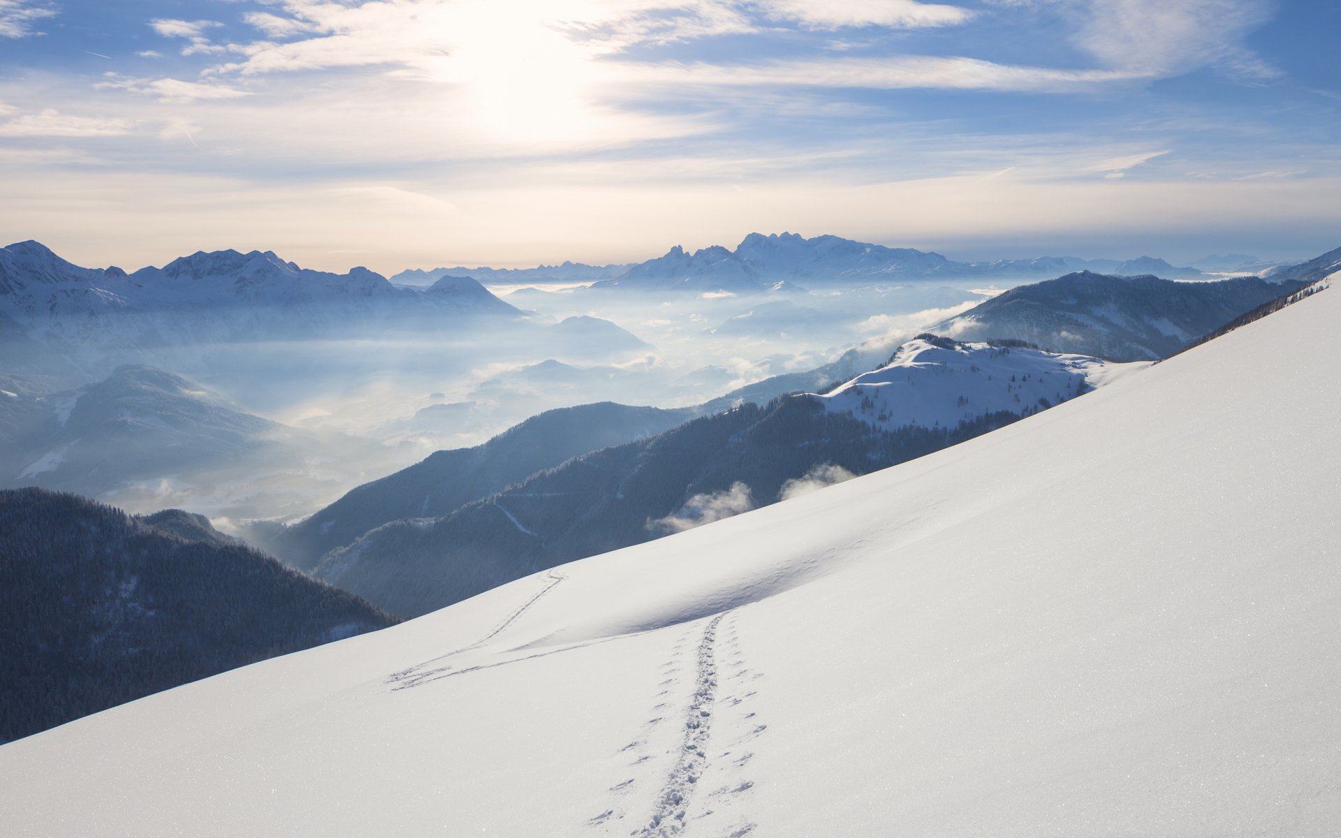 HD PC desktop wallpaper showcasing a serene snowy mountain landscape with fresh tracks in the snow under a bright sky, highlighting nature's beauty.
