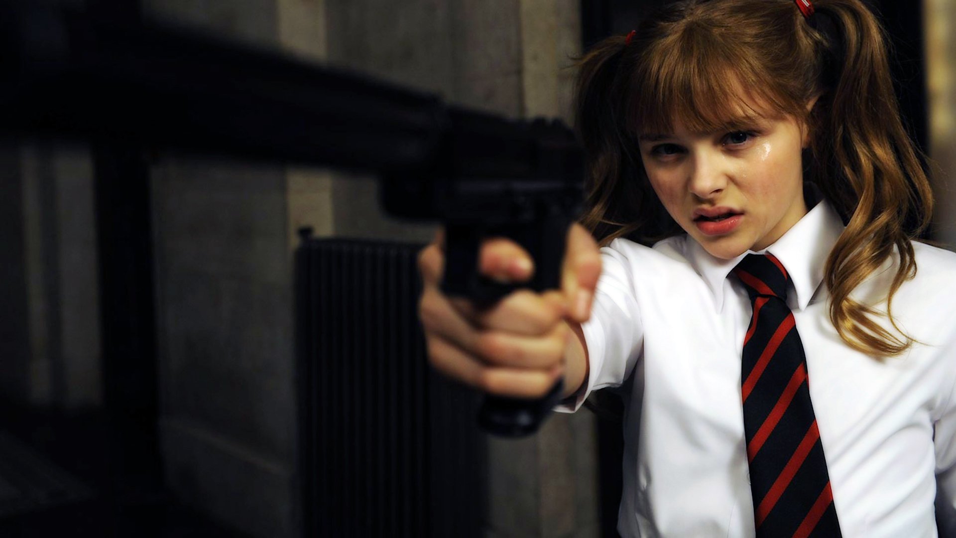 Chloë Grace Moretz wields a gun in a scene from the movie Kick-Ass, showcasing her character's fierce attitude. This HD image serves as a striking desktop wallpaper.