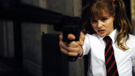 Chloë Grace Moretz wields a gun in a scene from the movie Kick-Ass, showcasing her character's fierce attitude. This HD image serves as a striking desktop wallpaper.