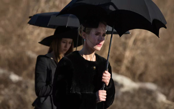 Two figures from American Horror Story: Coven walk solemnly with black umbrellas against a muted background, creating a haunting and atmospheric HD wallpaper for fans of the show.