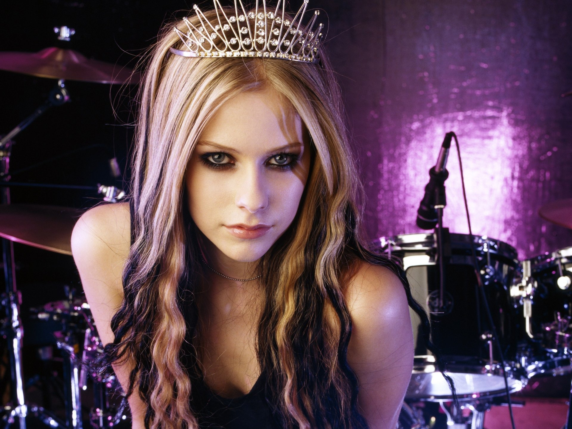 HD PC desktop wallpaper featuring Avril Lavigne with long blonde hair and a tiara, set against a purple-lit music studio backdrop with drums in the background.