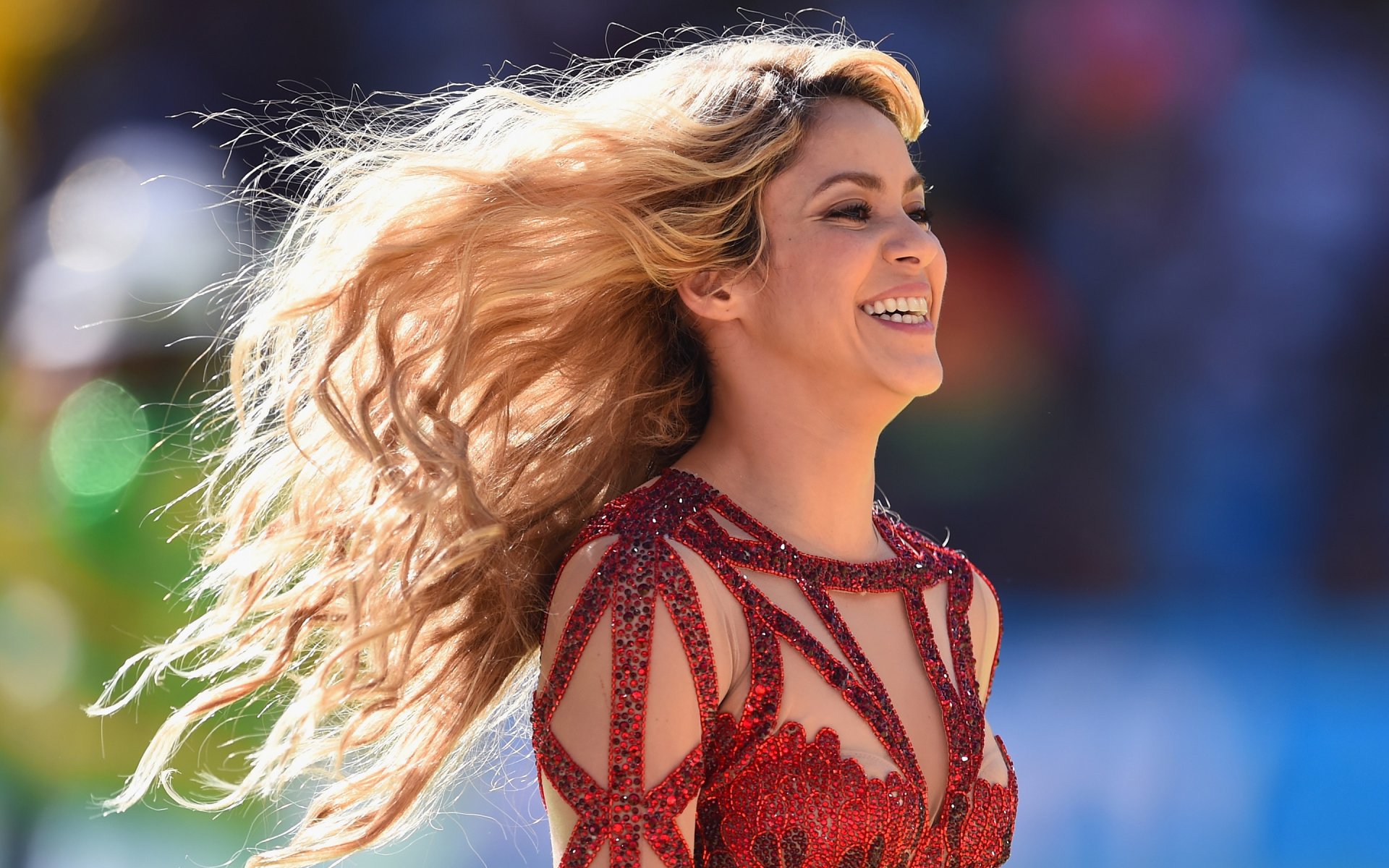 HD PC desktop wallpaper featuring Shakira smiling with flowing hair during a live music performance.