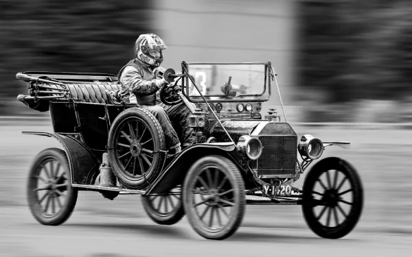Black-and-white HD desktop wallpaper showing a vintage Ford Model T vehicle in motion with a driver wearing protective gear.