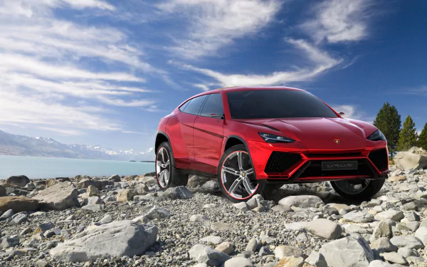 A striking red Lamborghini Urus parked on rocky terrain with a scenic backdrop of mountains and a lake, captured in high definition for a stunning desktop wallpaper.