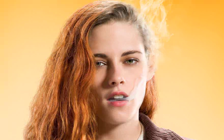 HD desktop wallpaper featuring American actress Kristen Stewart with green eyes, smoking, from the movie American Ultra against a warm yellow background.