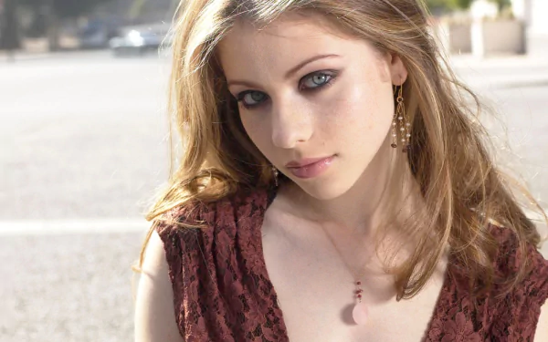 HD PC desktop wallpaper featuring celebrity Michelle Trachtenberg with soft makeup and wavy hair, wearing a brown textured top outdoors in natural light.