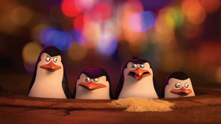 HD wallpaper featuring characters from the movie Penguins of Madagascar, with the four penguins standing in front of a colorful blurred background.