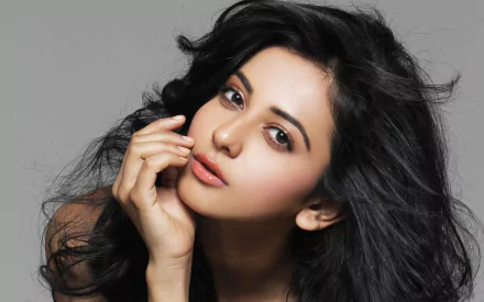 HD desktop wallpaper featuring celebrity Rakul Preet Singh with a natural makeup look and flowing dark hair, posing contemplatively against a neutral background.