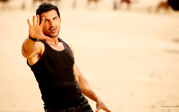 4K Ultra HD PC desktop wallpaper of a muscular man in a black tank top reaching toward the camera on a sunlit sandy beach.