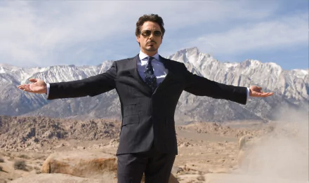 HD desktop wallpaper featuring Robert Downey Jr. in a scene from the movie Iron Man, standing with open arms in a desert landscape with mountains in the background.