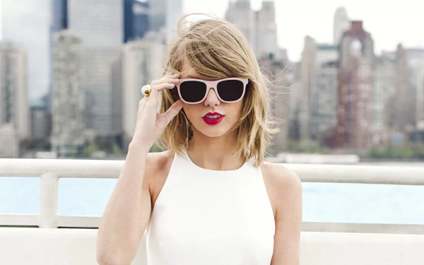HD wallpaper featuring Taylor Swift wearing sunglasses, set against a city skyline, capturing a stylish and confident vibe in a music-inspired atmosphere.