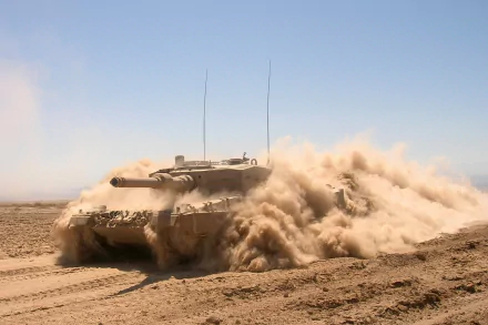 HD desktop wallpaper featuring a Leopard 2 military tank kicking up dust while maneuvering across a desert terrain under a clear sky.