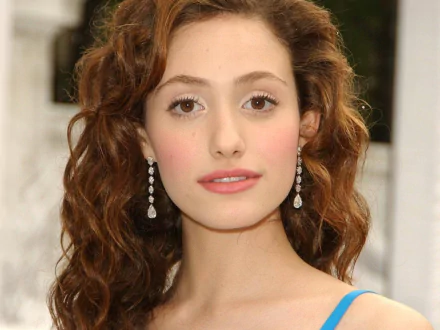 HD desktop wallpaper featuring a close-up portrait of celebrity Emmy Rossum with curly hair and dangling earrings against a blurred background.