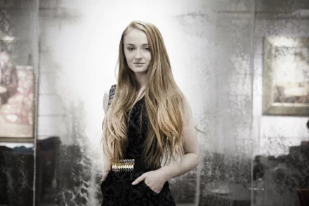 A stylish Sophie Turner stands confidently in a sleek outfit, surrounded by a softly blurred background, creating a captivating HD desktop wallpaper.
