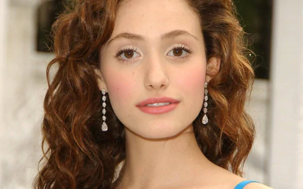 HD desktop wallpaper featuring a close-up portrait of celebrity Emmy Rossum with curly hair and dangling earrings against a blurred background.