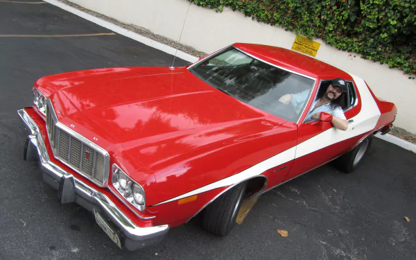 A vibrant red Ford Gran Torino parked on a sunny street, showcasing its classic design and sleek lines. This striking image serves as a 4K Ultra HD PC desktop wallpaper and background.