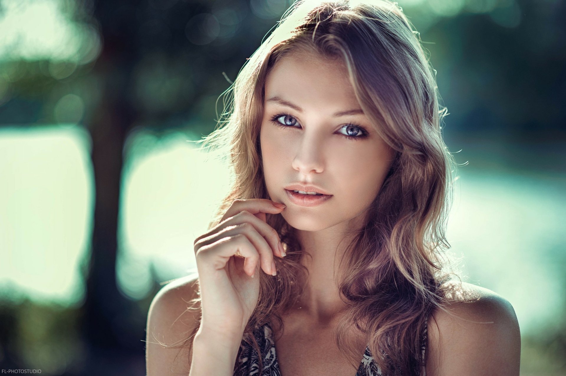 A beautiful woman with long, wavy hair poses thoughtfully against a serene outdoor background, creating an engaging HD desktop wallpaper.