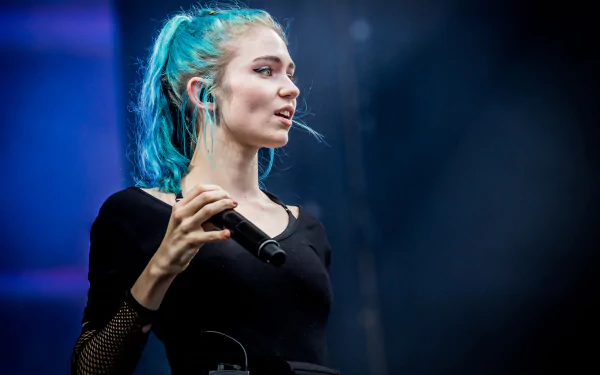 HD PC desktop wallpaper featuring a close-up of musician Grimes singing on stage with blue lighting in the background.