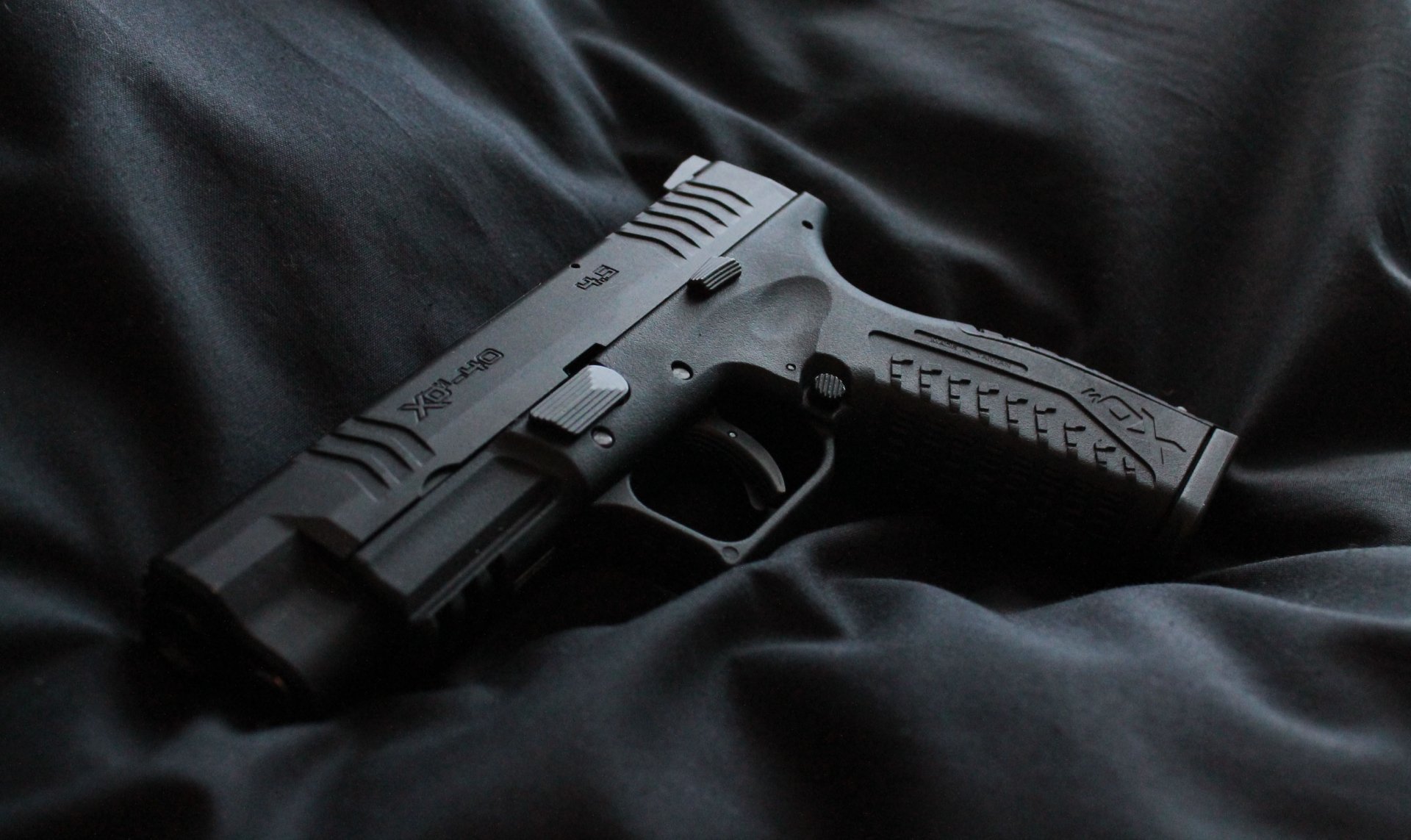 2K Quad HD PC desktop wallpaper showing a man-made black pistol resting on crumpled dark fabric, close-up high-contrast background.