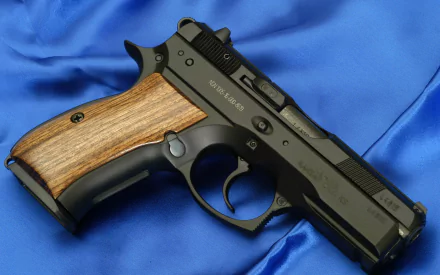 HD desktop wallpaper featuring a CZ 75 SP01 pistol with a black frame and wooden grip, displayed on a blue satin fabric background.