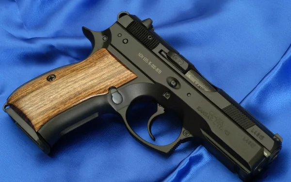 HD desktop wallpaper featuring a CZ 75 SP01 pistol with a black frame and wooden grip, displayed on a blue satin fabric background.