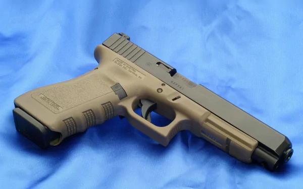 HD desktop wallpaper featuring a Glock pistol resting on a blue background. The firearm has a tan grip and a black slide, showcasing its detailed construction.