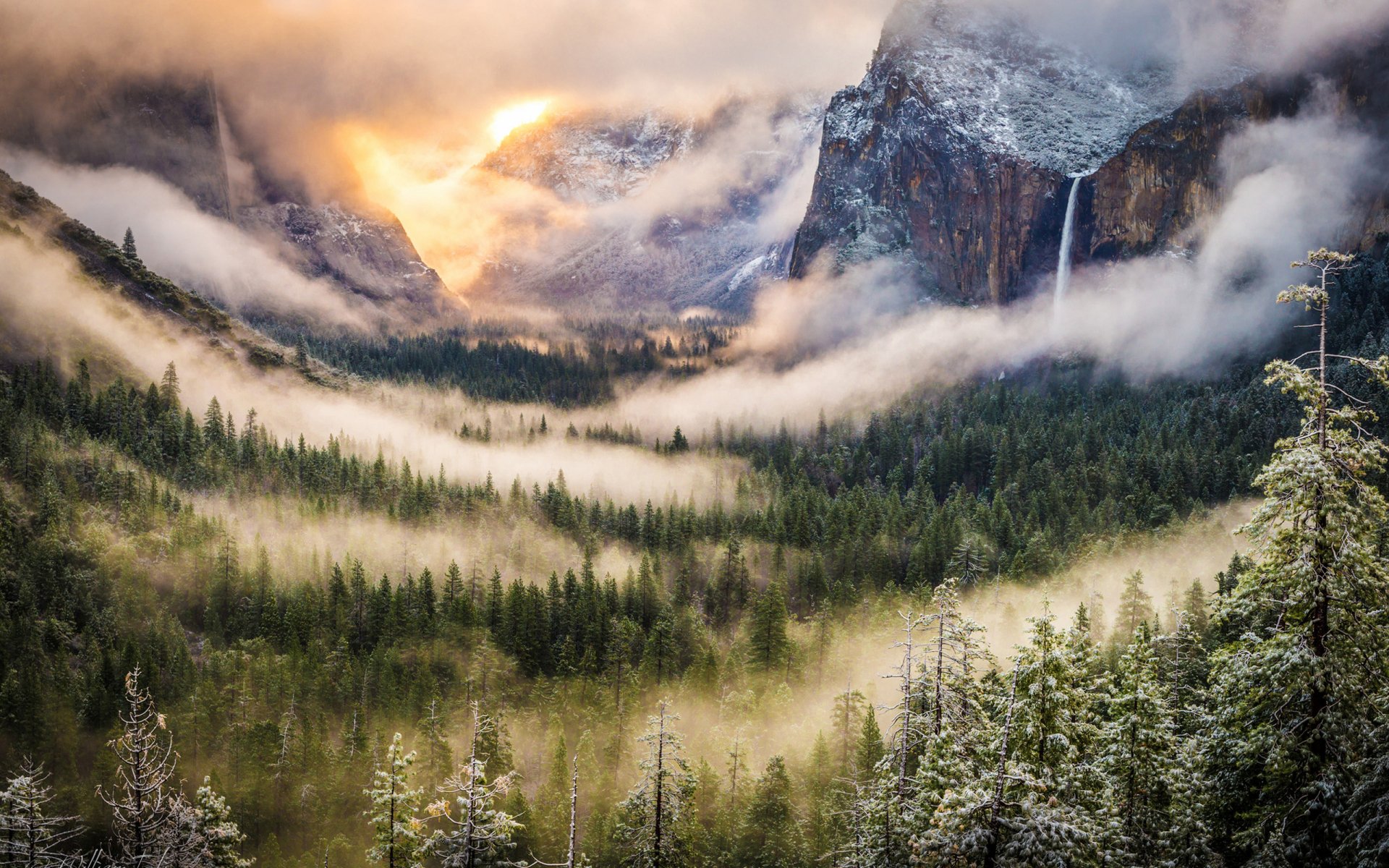 A serene landscape featuring a waterfall cascading through misty mountains at sunrise, surrounded by lush forests. This stunning HD wallpaper captures the beauty of nature.