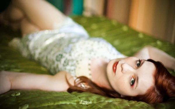 HD PC desktop wallpaper of a red-haired female celebrity reclining on a green satin surface, wearing a white lace dress and gazing at the camera.