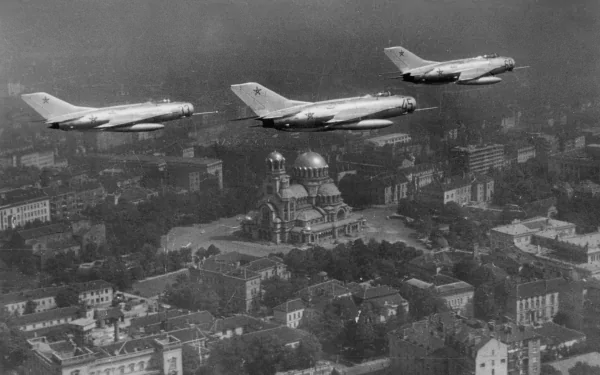 5K Ultra HD PC wallpaper: black-and-white scene of three Mikoyan-Gurevich MiG-19 military jets flying in formation over a city with a cathedral.