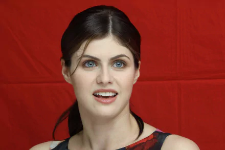 A high-definition wallpaper featuring actress Alexandra Daddario, showcasing her vibrant smile against a bold red background.
