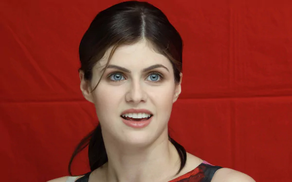A high-definition wallpaper featuring actress Alexandra Daddario, showcasing her vibrant smile against a bold red background.